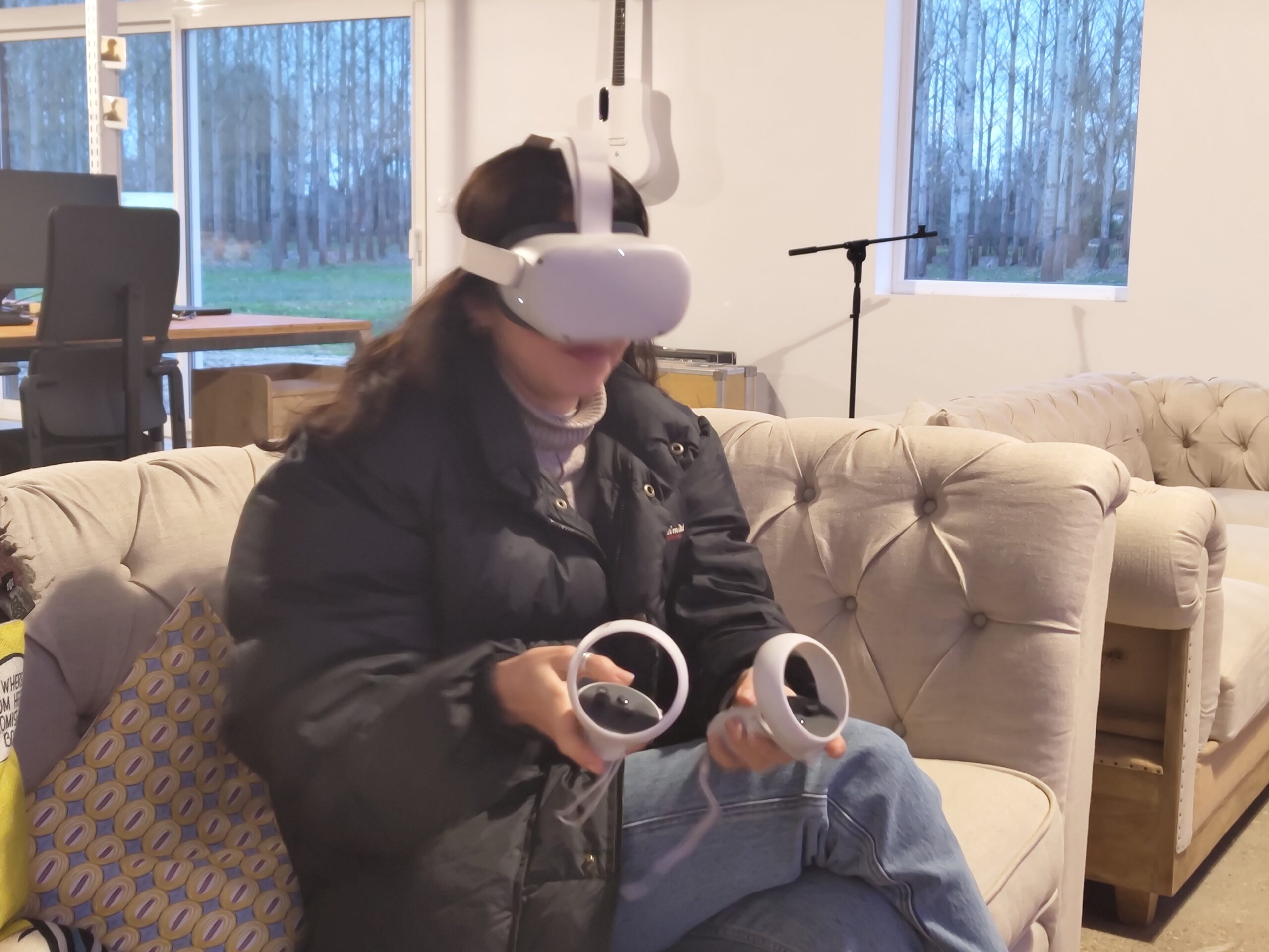 Visiteuse assise dans un salon, portant un casque Meta Quest et tenant ses manettes